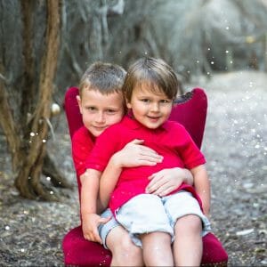 Two bothers cuddling on red chair for there Christmas Photos at Catherine Hill Bay